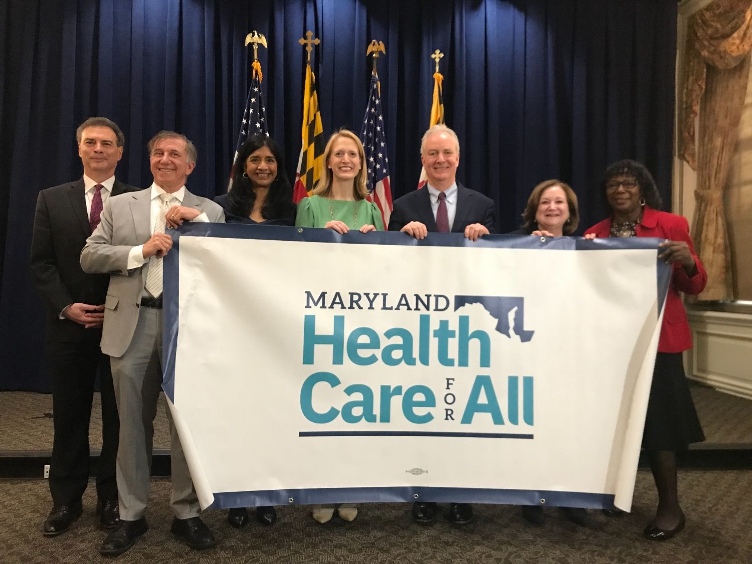 State and federal lawmakers and the Comptroller join Maryland Health Benefit Exchange and advocates for press conference. They stand behind a Health Care for All Coalition banner